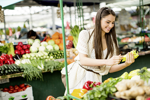 Frau auf einem Markt, umgeben von verschiedenen Obst und Gemüsesorten