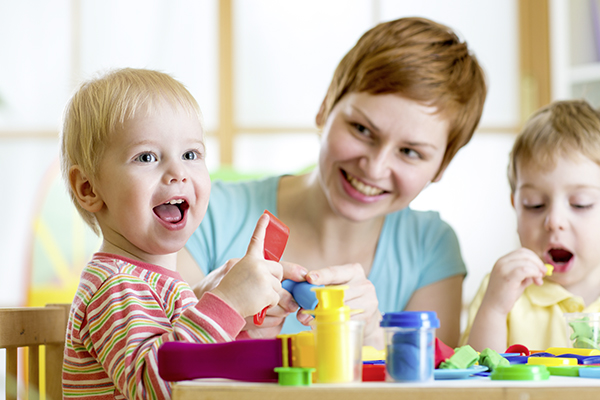 Erzieherin mit kurzen roten Haaren und 2 kleine Jungen spielen mit Bauklötzen